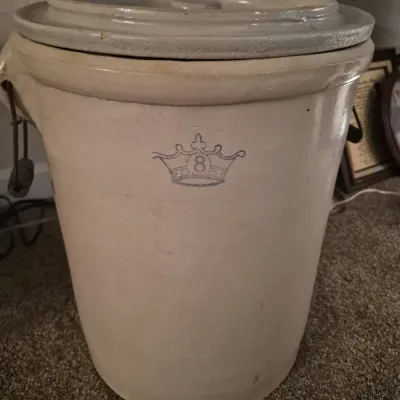 Vintage 8-gallon stoneware crock with lid and wire bail handles, featuring a blue crown mark on the front.