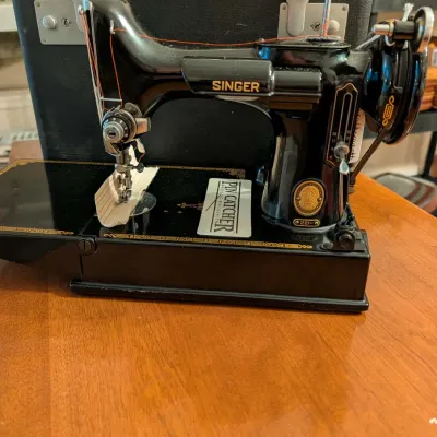 Vintage Singer Featherweight 221 portable electric sewing machine in a black finish, accompanied by its hard carrying case.