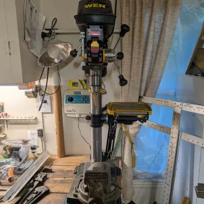 WEN benchtop drill press with an attached step drill bit and a heavy-duty swivel vise mounted to a wooden workbench.