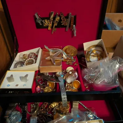 Vintage jewelry box filled with costume jewelry, tie clips, cufflinks, brooches, and wristwatches.