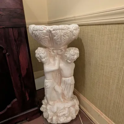 Vintage white cast plaster or concrete birdbath featuring three cherubs supporting a leaf-motif bowl, marked "MEXICO" on the base.