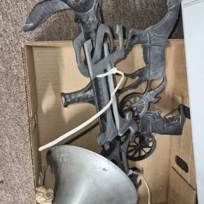Disassembled cast metal dinner bell and wall mount bracket featuring a horse and buggy motif.