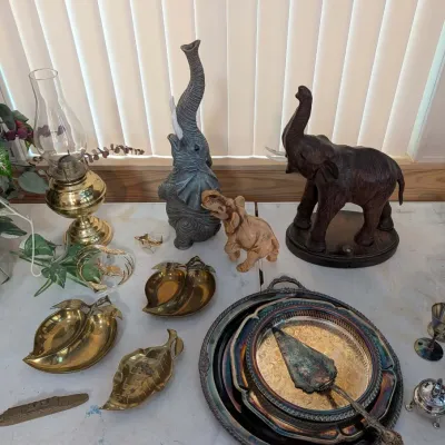 Collection of decorative household items including elephant figurines, brass leaf-shaped dishes, silver-plated serving trays, a brass oil...