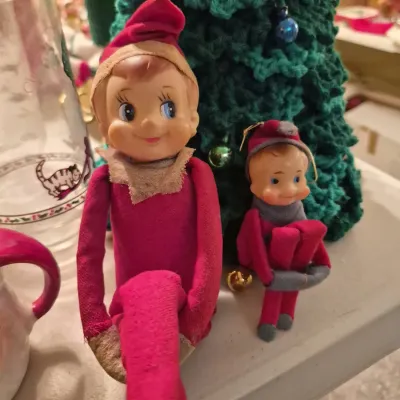 Vintage knee-hugger elf dolls with vinyl painted faces and felt bodies, shown beside a crocheted yarn Christmas tree.