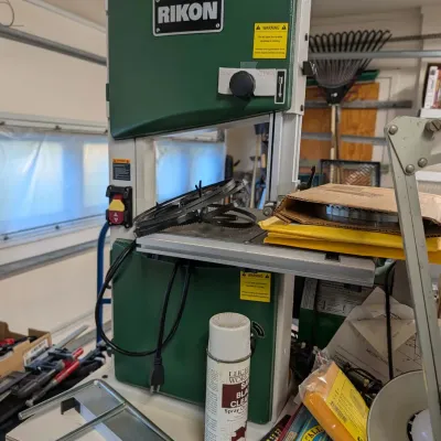 Green Rikon woodworking band saw, accompanied by spare saw blades and various workshop tools and accessories.