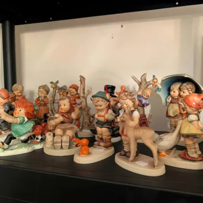 Collection of vintage porcelain Hummel and similar German-style children figurines arranged on a shelf.