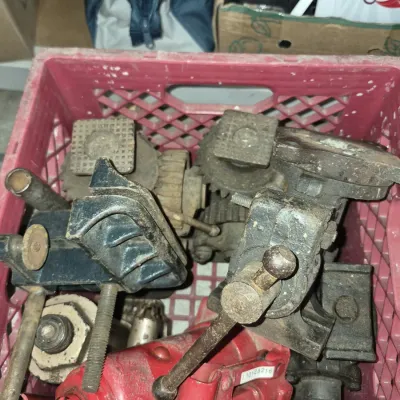 Red plastic crate filled with assorted vintage metal tools, including mechanical jacks, pipe vices, and heavy-duty clamps.