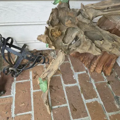 Natural driftwood sculpture with faux foliage accents, paired with a wrought iron cage-style planter on a brick patio.
