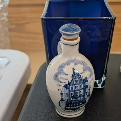 Vintage KLM Delft blue ceramic house decanter with cork stopper, dated 1959, shown in front of a square cobalt blue glass vase.
