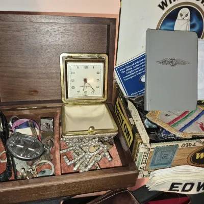 A vintage wooden jewelry box filled with various trinkets, including a Westclox travel alarm clock, rhinestones, and pins, beside a White...