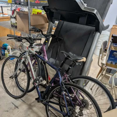Two Schwinn hybrid bicycles parked in front of a folded, upright motorized treadmill in a storage area.