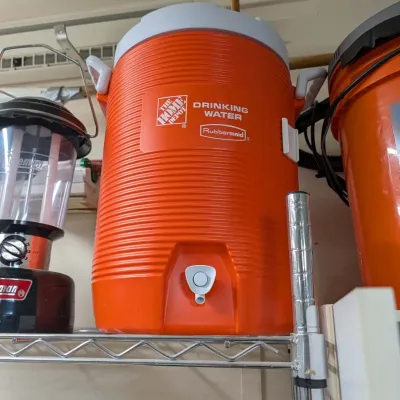 Orange Rubbermaid 5-gallon Home Depot drinking water cooler dispenser, displayed on a wire storage rack.