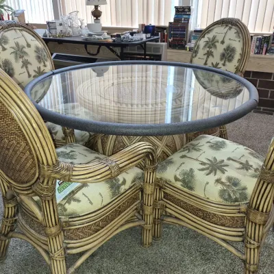 Tropical style wicker and rattan dining set featuring a round glass-top table and four matching armchairs with palm tree patterned...