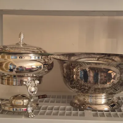 Polished silver-tone chafing dish with pineapple finial lid alongside a matching pedestal punch bowl.