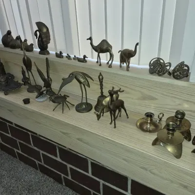 Collection of vintage brass decor items including bird figurines, camels, elephants, deer, bells, and candlesticks displayed on a shelf.