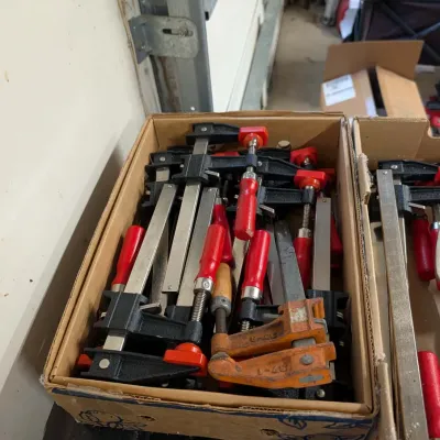 Cardboard box filled with assorted bar clamps and F-style woodworking clamps featuring red and orange handles.