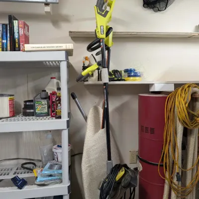 Ryobi 40V cordless string trimmer hanging on a garage wall, surrounded by various lawn care accessories, a central vacuum unit, and...