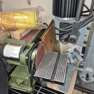 Central Machinery benchtop belt and disc sander alongside a grey drill press stand and accessories.