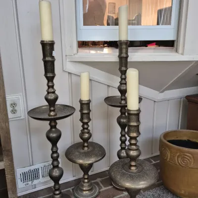 Set of four tall vintage brass floor-standing candlesticks featuring intricate engraved detailing and drip trays, complete with white...