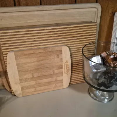 Collection of wooden and bamboo cutting boards stacked alongside a clear glass footed bowl filled with metal cookie cutters and mini...