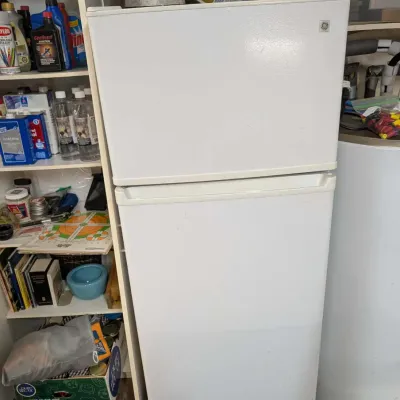 White GE top-freezer refrigerator mounted on a rolling dolly base.