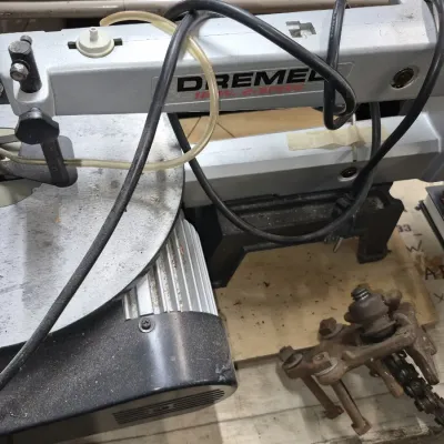 Dremel 15-inch 2-speed scroll saw with attached power cord and a small rusted mechanical part on a workbench.