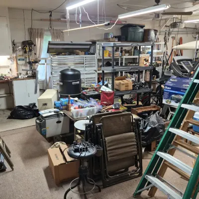 Workshop and garage filled with various tools, shelving units, ladders, patio chairs, and a vertical smoker.