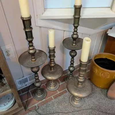 Set of four ornate etched brass floor candlesticks in varied heights, each topped with a cream-colored pillar candle.
