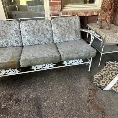 Sale Photo Thumbnail #182: Vintage white wrought iron patio sofa and matching side table featuring decorative floral scrollwork and weathered floral cushions.