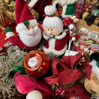 Sale Photo Thumbnail #14: Collection of assorted Christmas decorations and figures, featuring plush Santa and Mrs. Claus dolls, metallic ornaments, a faux cardinal, and festive ribbons.