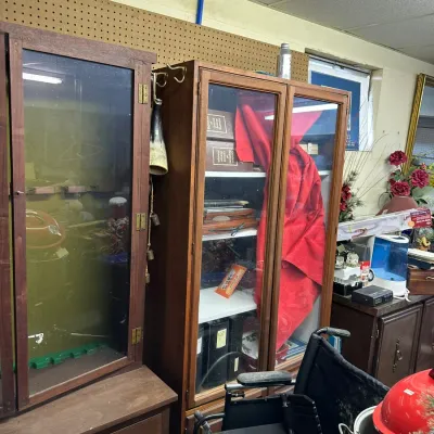 Sale Photo Thumbnail #319: Two vintage wooden display cabinets standing alongside a wheelchair, small appliances, and household decor.