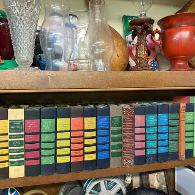 Sale Photo Thumbnail #65: Collection of vintage Reader's Digest Condensed Books lined up on a wooden shelf below glassware and decor items.