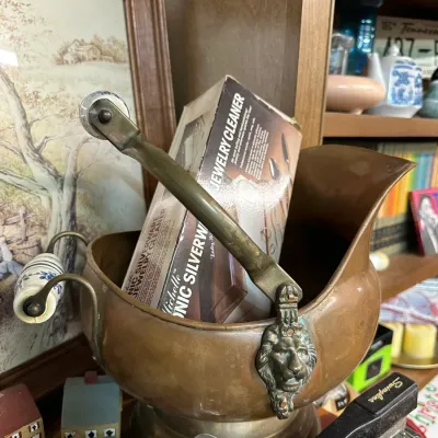 Sale Photo Thumbnail #57: Vintage copper scuttle bucket featuring a lion head motif and a ceramic-handled swing handle. A boxed Michelle sonic silverware and jewelry cleaner rests inside.