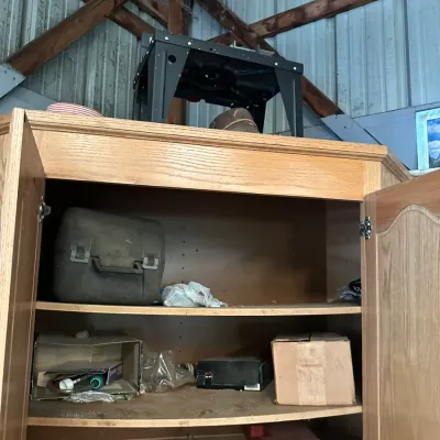 Sale Photo Thumbnail #498: Large wooden cabinet with open doors filled with various tools, boxes, and workshop supplies, topped with a black power tool stand.
