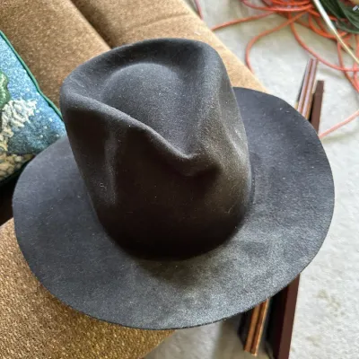 Sale Photo Thumbnail #636: Dark brown or black felt fedora hat featuring a creased crown and wide brim, showing minor dust and surface wear.