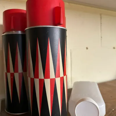 Sale Photo Thumbnail #90: Pair of vintage aerosol cans featuring a bold red, black, and cream geometric diamond pattern with red plastic caps.