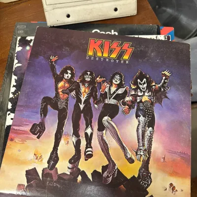 Sale Photo Thumbnail #133: Vintage KISS Destroyer vinyl record album sleeve featuring the band's iconic painted cover art, resting atop a stack of records.
