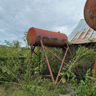 Sale Photo Thumbnail #340: Vintage elevated metal fuel storage tank on an A-frame metal stand, showing heavy weathering and surface rust.