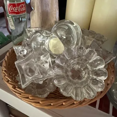 Sale Photo Thumbnail #238: Collection of clear glass candle holders in various shapes, including floral, star, and heart designs, arranged in a shallow woven basket.