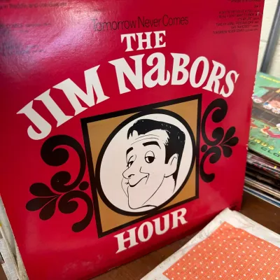 Sale Photo Thumbnail #134: Vintage "The Jim Nabors Hour" vinyl LP album, featuring prominent red cover artwork with an illustrated portrait.