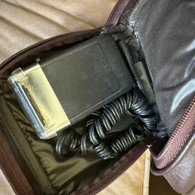 Sale Photo Thumbnail #618: Vintage electric shaver with coiled power cord stored in a brown zippered travel case.