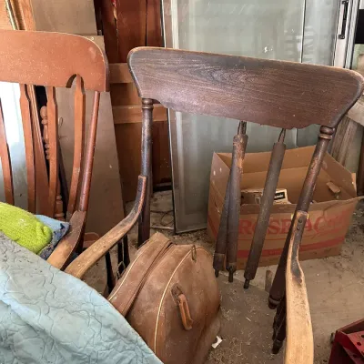 Sale Photo Thumbnail #722: Vintage dark stain wooden armchair with spindle backrest displaying significant wear, accompanied by a distressed brown leather bag.