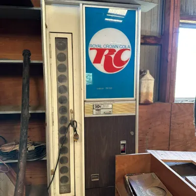 Sale Photo Thumbnail #538: Vintage Royal Crown Cola vending machine with woodgrain lower panel and 50-cent coin mechanism, showing light cosmetic wear.