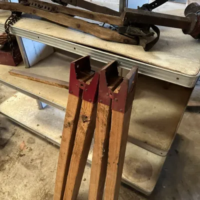 Sale Photo Thumbnail #214: Set of four wooden sawhorse legs with red metal brackets, alongside vintage hand tools resting on a work table.