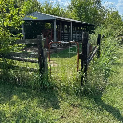 Sale Photo Thumbnail #473: Rustic wire and metal farm gate set between wooden fence posts, with a pole barn structure visible in the background.