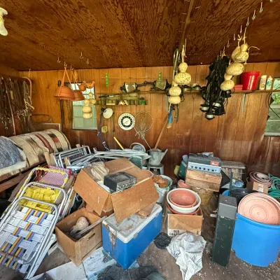 Sale Photo Thumbnail #272: A workshop and shed space packed with miscellaneous items, including vintage lawn chairs, a blue cooler, planters, electronics, hanging gourds, and horse tack.