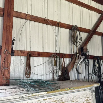 Sale Photo Thumbnail #469: Assorted workshop items and farm hardware, including wire coils, ropes, extension cords, and tomato cages hanging on a pole barn wall.