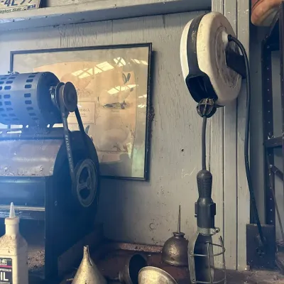 Sale Photo Thumbnail #493: Vintage workshop collection including a wall-mounted retractable trouble light, motorized belt-driven machine, metal oil funnels, an oil can, and Tennessee license plates from the late 1980s.