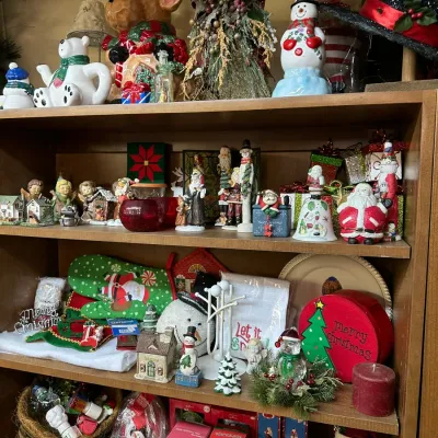 Sale Photo Thumbnail #49: A wooden bookcase packed with various Christmas decor items, including Santa figurines, snowmen, holiday tableware, ceramic teapots, and boxed ornaments.