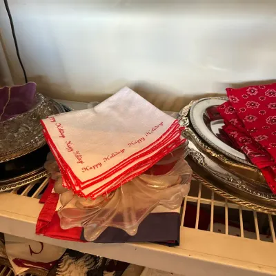 Sale Photo Thumbnail #680: Selection of vintage linens including white embroidered 'Happy Holidays' napkins, red bandana print cloth napkins, and various silver-plated serving trays.